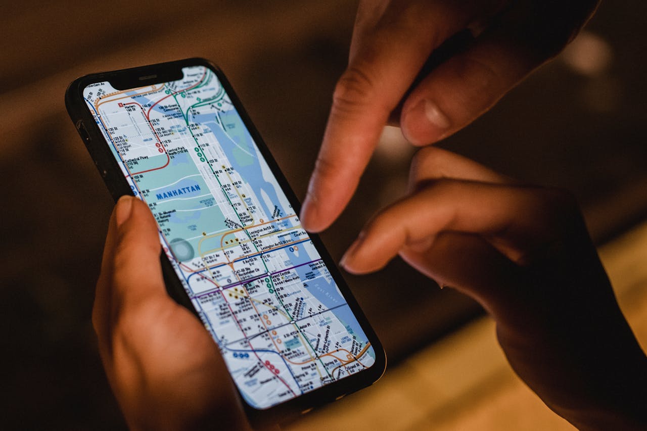 Close-up of hands using a smartphone with a New York City subway map at night, highlighting modern navigation.